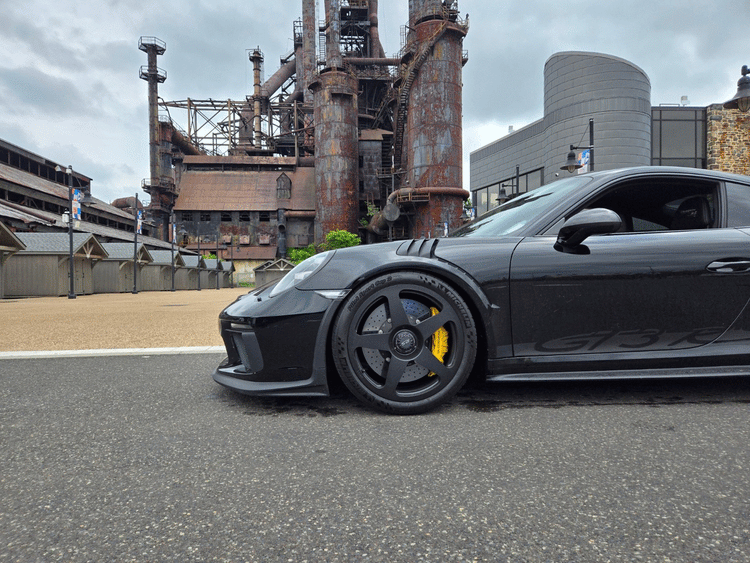 Side of a black Porsche in front of an industrial old factory.