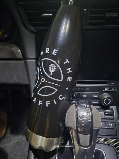 Black We Are The Traffic water bottle in the interior of a car next to the shift knob.